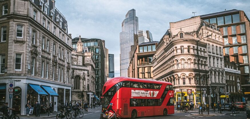 Red double-decker bus on a London street with historic City of London buildings and skyscrapers